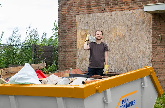 Aannemer gooit puin in een container tijdens de verbouwing