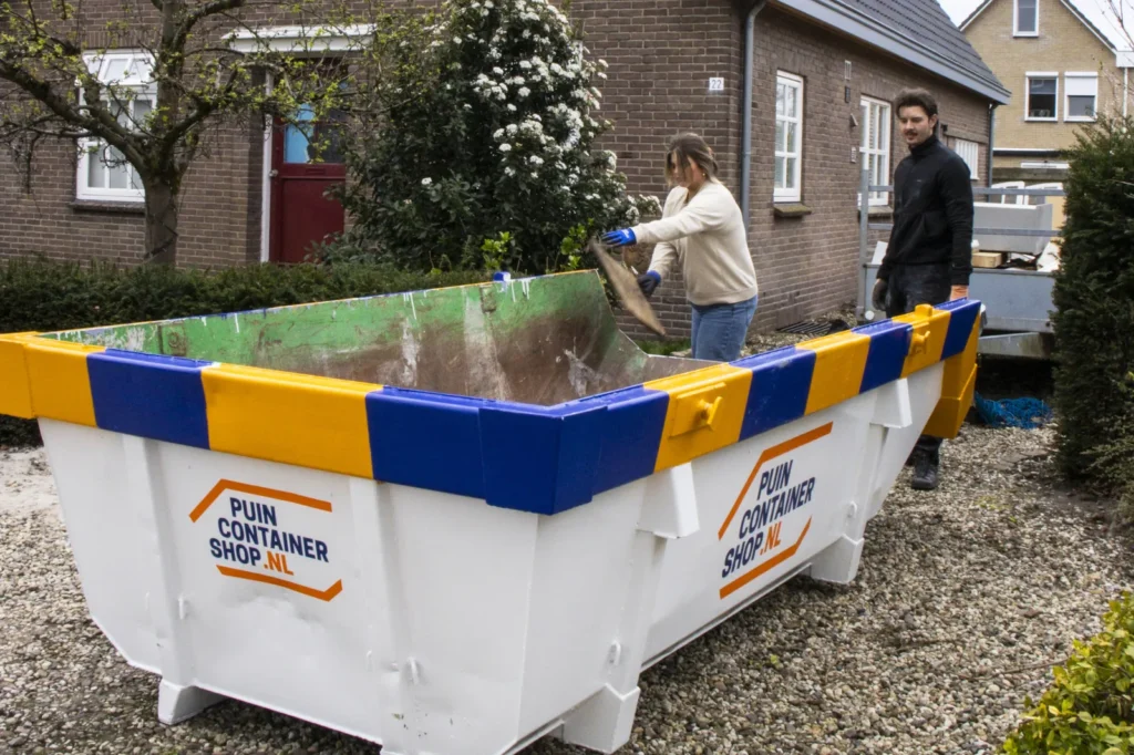 Vrouw gooit bouwafval in een afzetcontainer van Puincontainershop.nl naast een woning