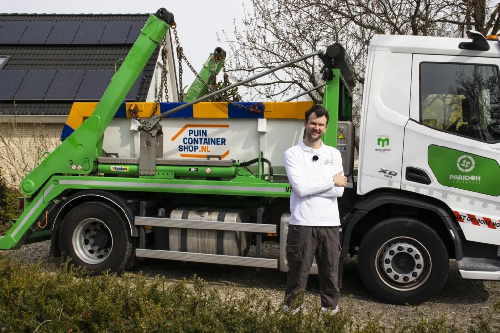 Medewerker van Puincontainershop.nl bij de kraanwagen met een afzetcontainer op de laadbak